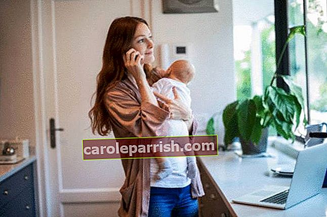 Brünette-Frau-lächelt-mit-ihrem-Neugeborenen-in-ihrer-sauberen-weißen-Küche