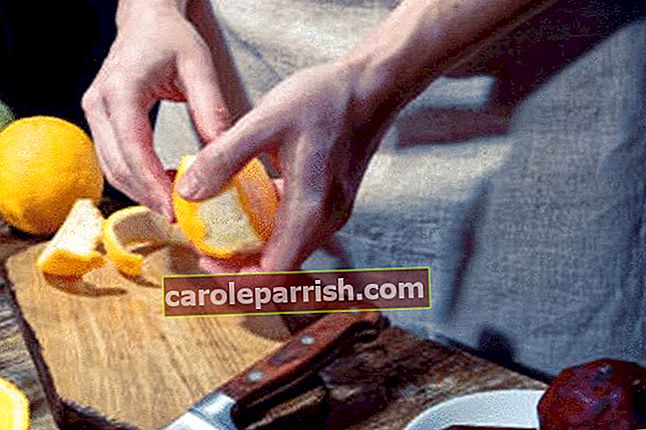 männliche Hand schält einen orangefarbenen Keil über einem großen Messer